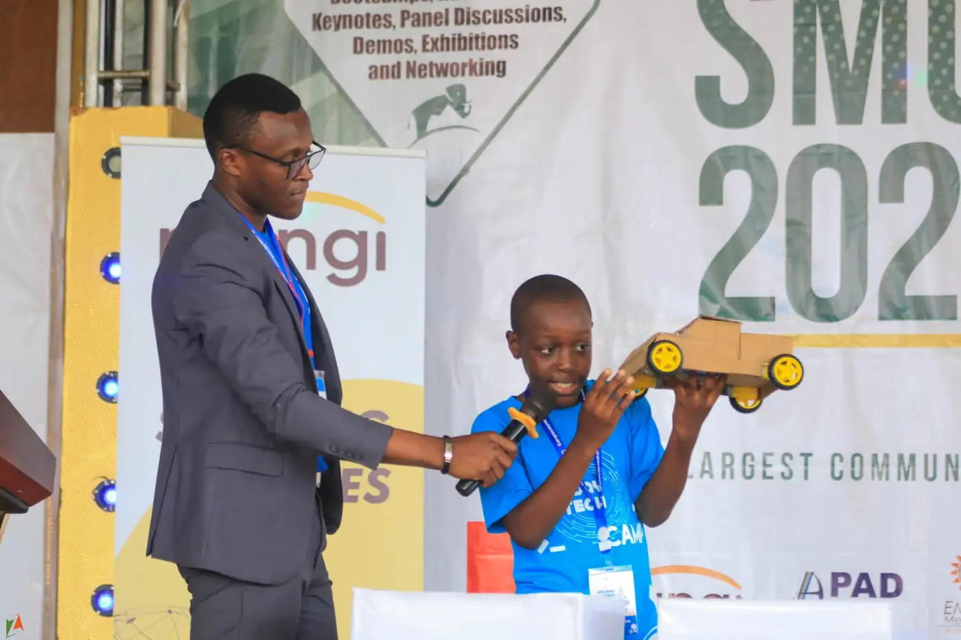A young builder demonstrating a model car on stage